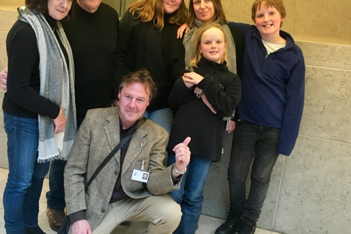 Group of seven people posing indoors, with one kneeling in front.