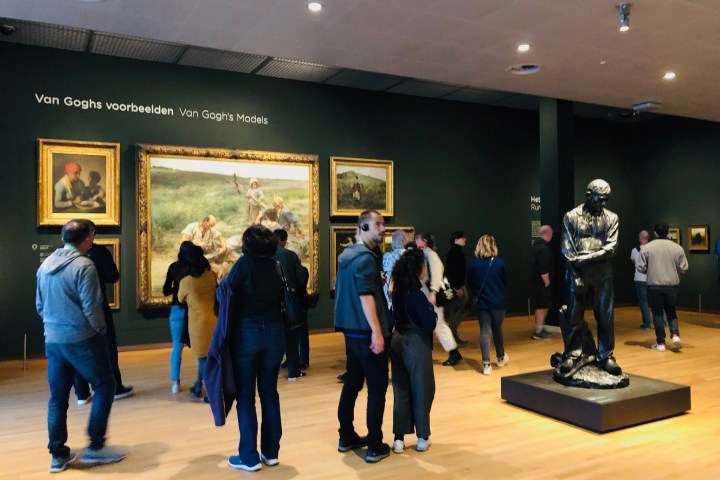 People viewing paintings and a statue at an art exhibit titled 'Van Gogh's Models'.
