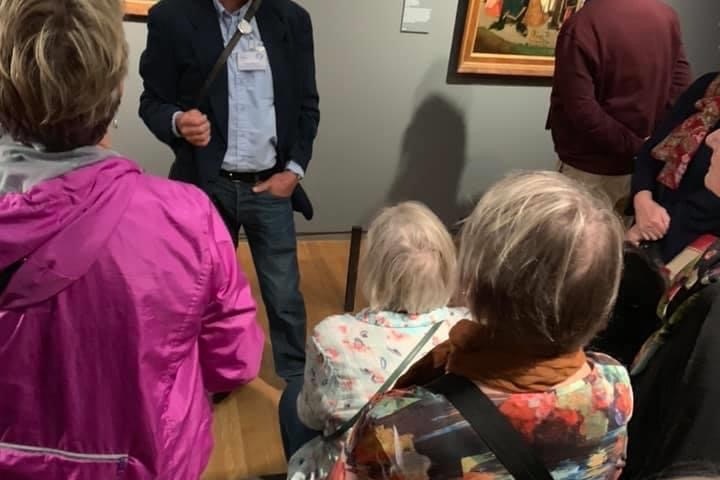 A group of people in a museum gallery viewing and discussing artwork on the walls.