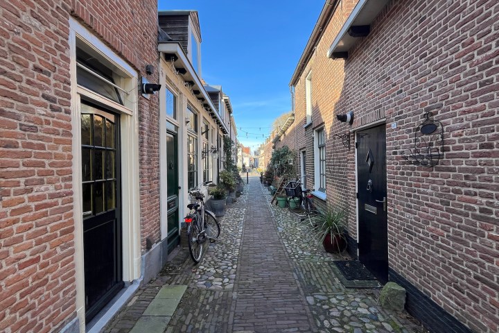 Narrow cobblestone alleyway between red-brick buildings under a clear blue sky.
