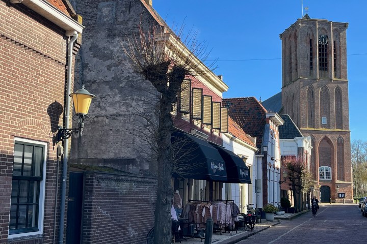 Street view with brick buildings, a church tower, and a clear blue sky.