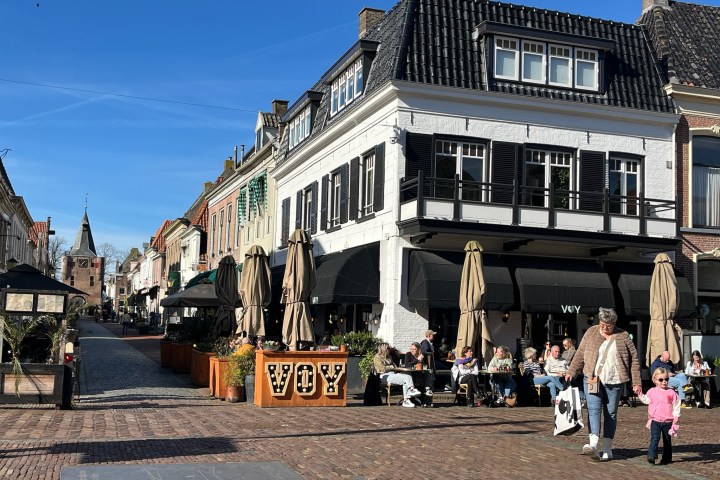 People dining outside a cafe on a sunny street with historic buildings.