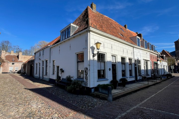 Corner view of old brick buildings with red roofs on a cobblestone street under a clear blue sky.