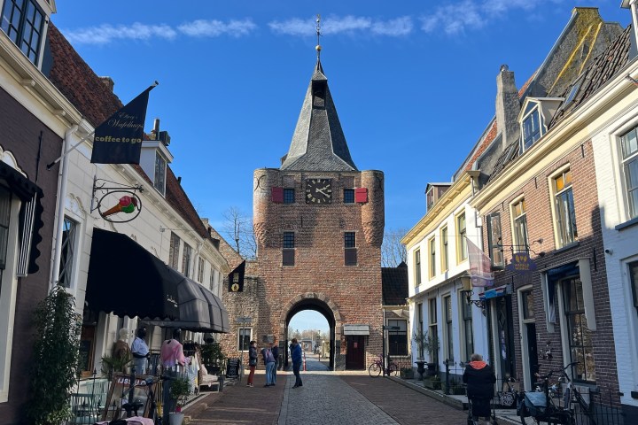 Historic brick gate tower with clock, flanked by charming shops on a sunny street.