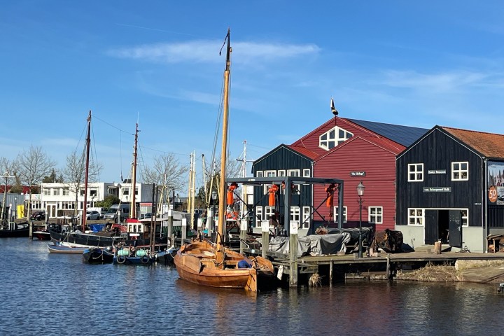 Boats docked by colorful wooden buildings on a sunny day at a marina.