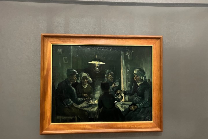 Framed painting of people dining around a table under dim lighting.