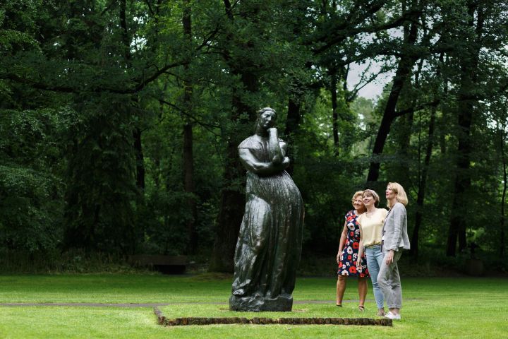 Three people admire a tall statue in a forested park setting.