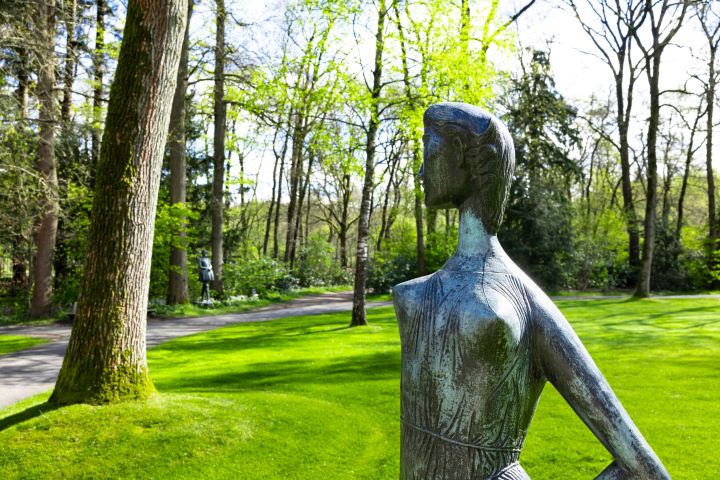 Statue of a woman in a park surrounded by trees and green grass.