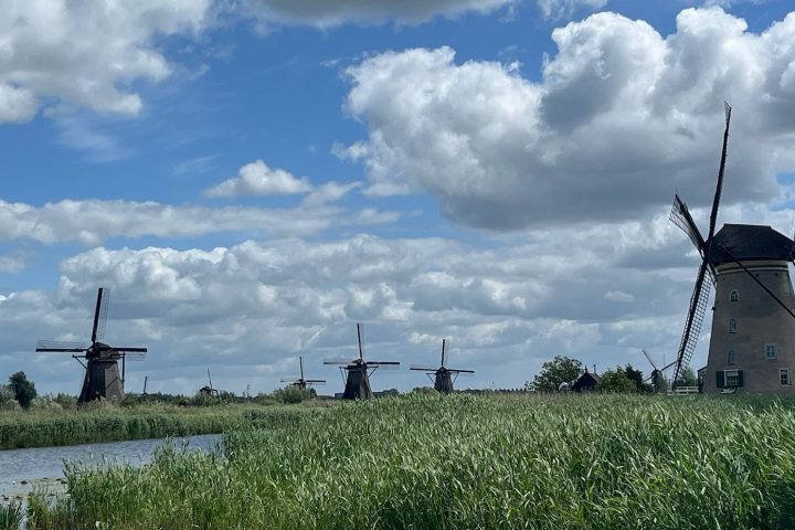 Windmills by a river under a cloudy sky.