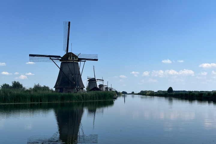Windmills by a calm river under a clear blue sky.